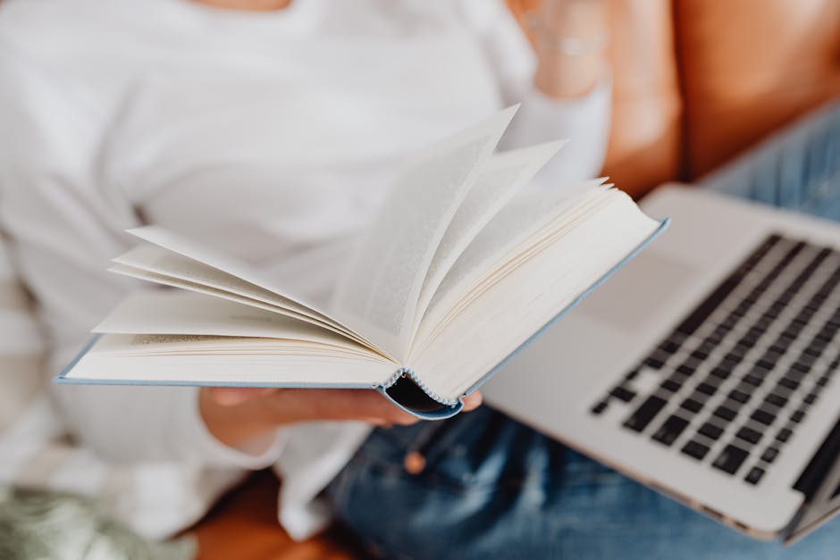 Person enjoying leisure time with a book and laptop indoors. A cozy reading setup.