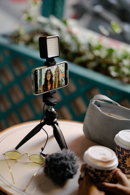 Two young vloggers recording a video blog in a café, enjoying coffee together with a smartphone and tripod setup.